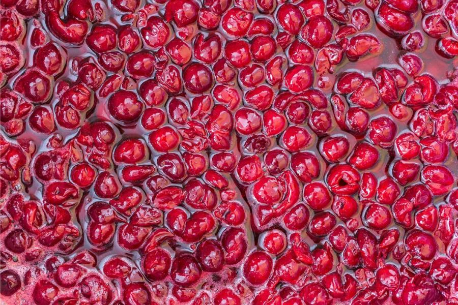 Vista superior de cerezas de color rojo vibrante en un jarabe espeso y brillante, con las cerezas empaquetadas juntas y algunas ligeramente machacadas, creando una superficie rica y texturizada.