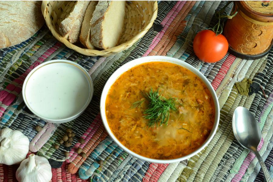 Un cuenco con shchi, una sopa tradicional rusa de col, adornada con eneldo fresco sobre un mantel de colores. 