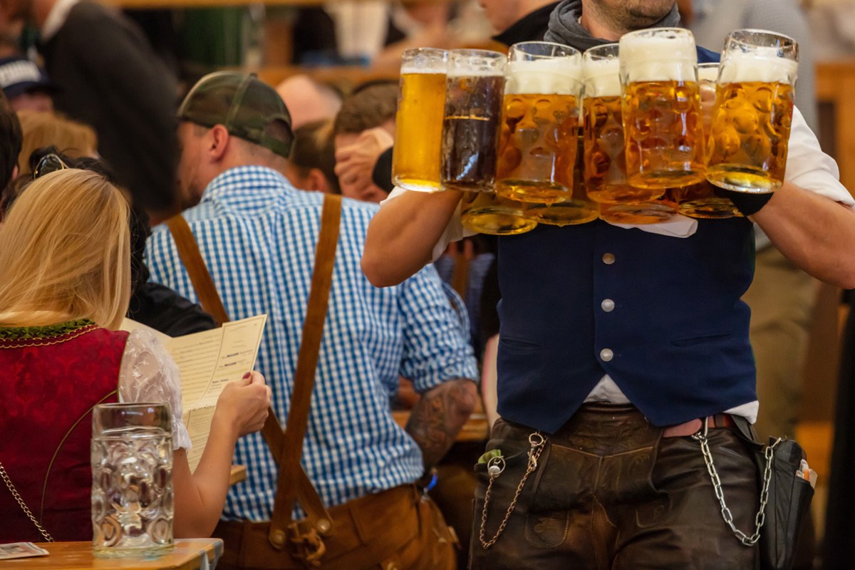 Oktoberfest, Munich, Germany. Un camarero sirvinedo cerveza en primer plano con gente vestida con el atuendo bávaro tradicional alrededor.