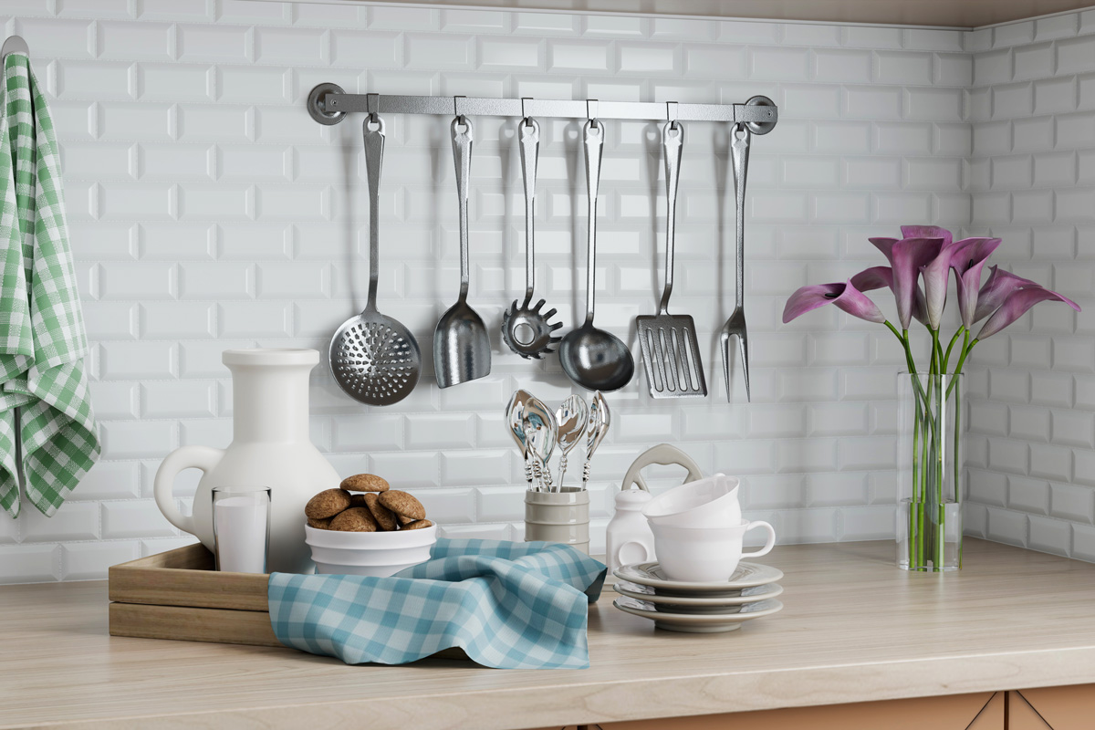 En una cocina contemporánea, una colección de utensilios de cocina de acero inoxidable cuelga de la pared. Un paño de cocina a cuadros, flores coloridas y platos añaden encanto al ambiente.