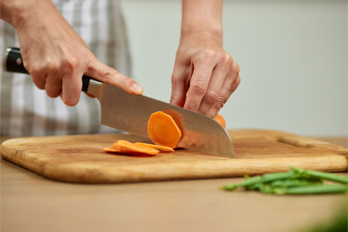 Una persona cortando zanahoria con un cuchillo santoku sobre una tabla de madera.