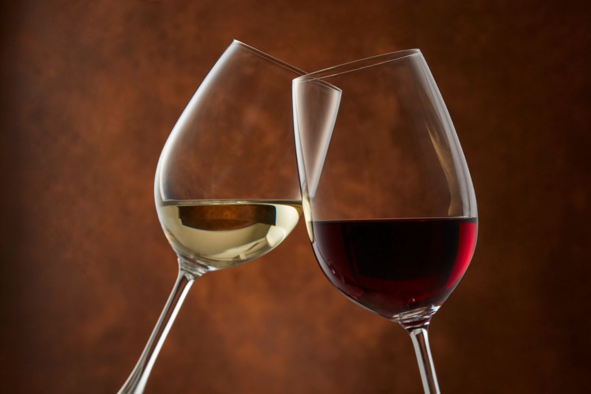 Una copa con vino blanco y otra copa con vino tinto contra un fondo oscuro.