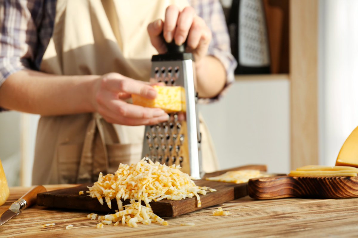 Un hombre rallando queso con un rallador de caja.